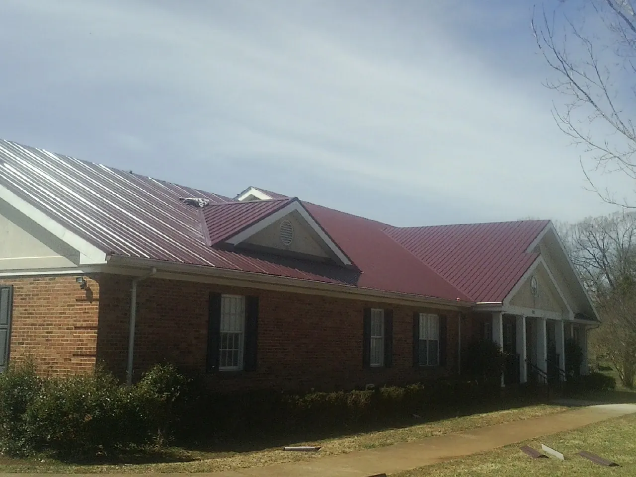 Red metal roof with gabled entries on a long brick building, from a Hail Damage Roof Repair job in Huntly