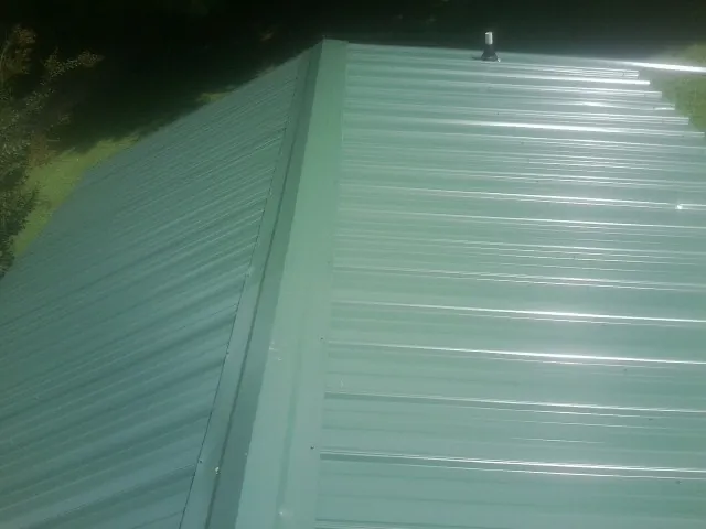 New green metal panels meeting at the ridge of a roof — Flat Roof Repair work by our crew in Huntly