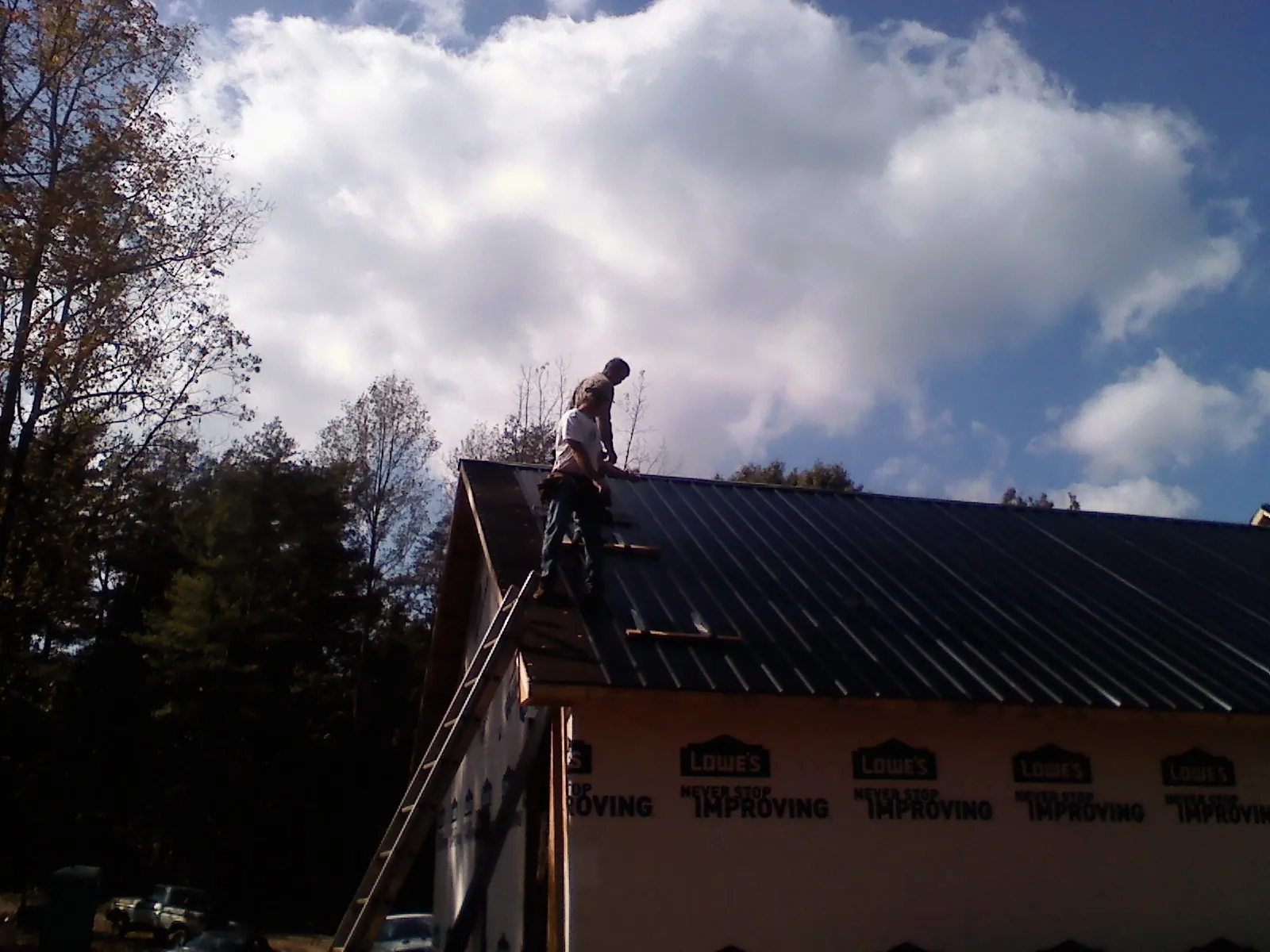 Roofer fastening dark metal panels high against a cloudy sky, from a Roof Inspection job in Huntly