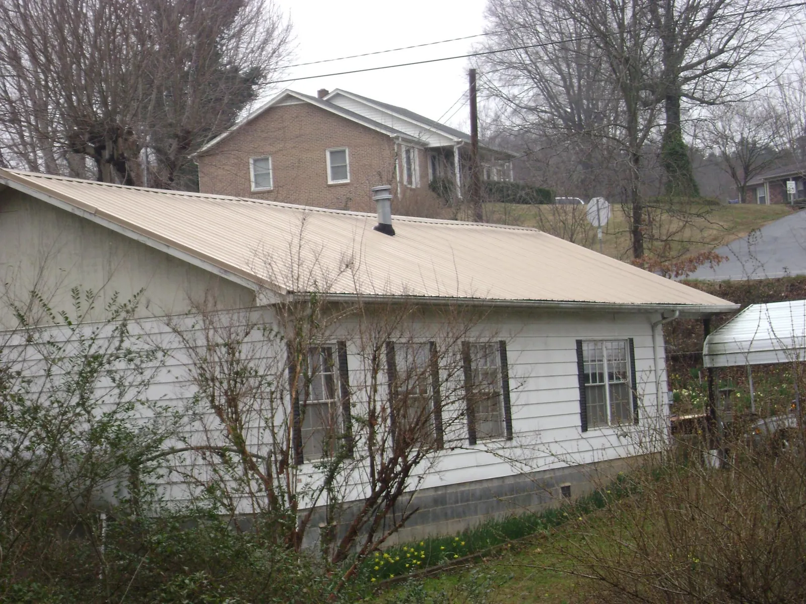 Tan metal roof on a white sided house set into a hillside — Commercial Roofing by Roofing Brothers in Huntly