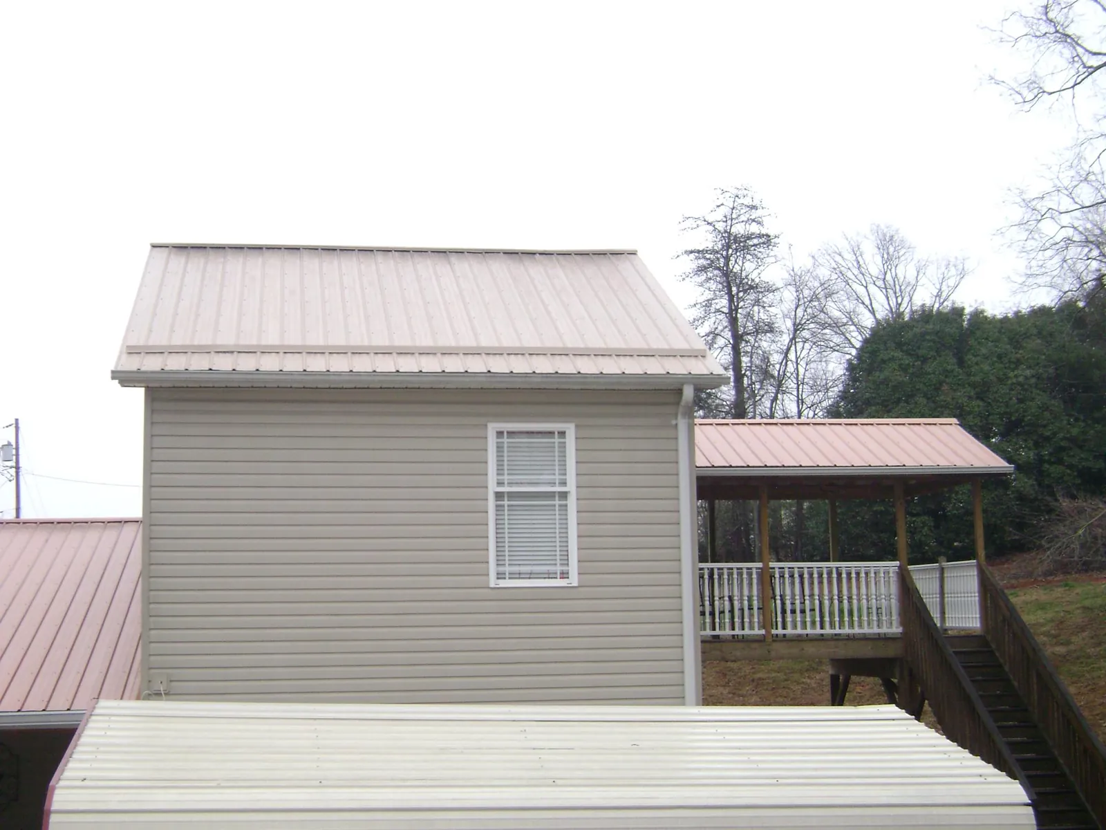 Tan metal roofs on a two story addition and attached porch, from a Roof Replacement job in Huntly